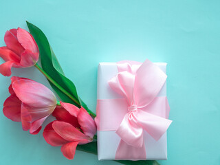 Beautiful delicate flowers with a gift box and a satin ribbon bow on a blue background. Flower card, women's Day