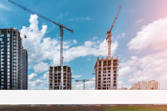 Blank white long information banner fixed on construction site hoarding under working cranes against blue sky