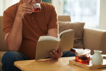 Cropped image of old man enjoying cup of tea and good book