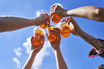 Low angle view of hands toasting beer on blue sky at festival