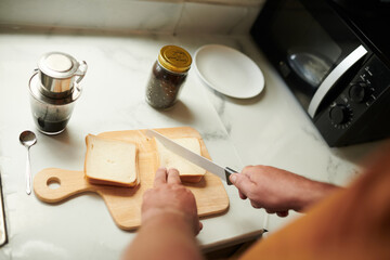 Hands of man cutting bread in triangles when making sandwiches for breakfast