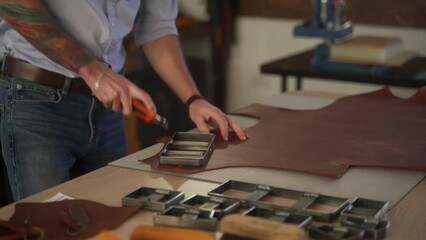 Leather craftsman works in his workshop. Master making leather products. Man carves leather sheet shape for die punch cutter leather punching knife. Male fits on craft cutting mold.