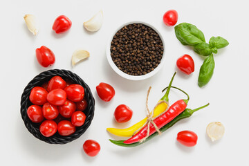 Cherry tomatoes in black basket, green basil leaves and chili pepper on white background.