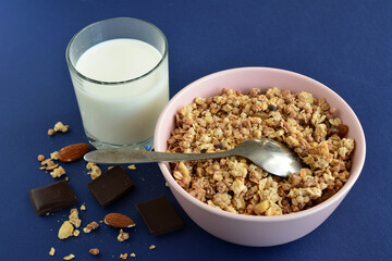 chocolate and banana muesli in pink bowl with spoon and glass of milk, close-up