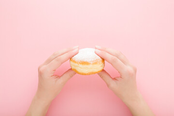 Young adult woman hands holding fresh donut with sprinkled sugar on light pink table background....