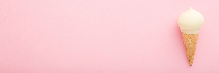Waffle cone of white vanilla ice cream on light pink table background. Pastel color. Wide banner. Closeup. Cold sweet snack in summer. Empty place for text. Top down view.