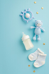 Baby accessories concept. Top view vertical photo of socks teether milk bottle knitted teddy-bear toy and gold stars on isolated pastel blue background