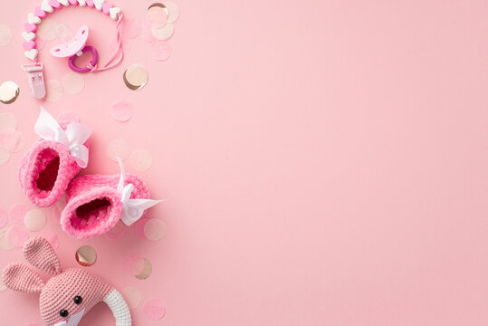 Baby accessories concept. Top view photo of pacifier chain pink booties knitted bunny rattle toy and shiny confetti on isolated pastel pink background with copyspace