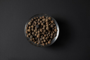 allspice (pimento) in a glass bowl isolated on black background 