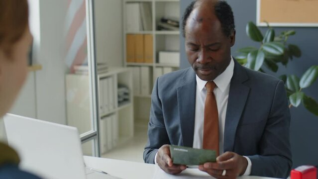 African American consular officer checking passport of visa applicant during interview in US embassy