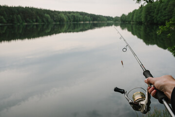 Fisherman with rod, spinning reel on the river bank. Fishing for pike, perch, carp. Fog against the backdrop of lake. background Misty morning. wild nature. The concept of a rural getaway.