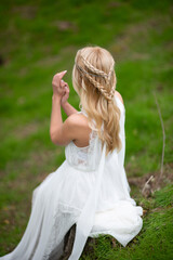 Fototapeta na wymiar Beautiful blonde woman in a white dress with a chic hairstyle in nature, rear view