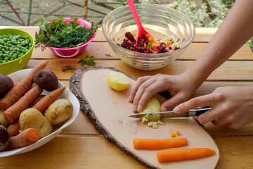 Russian vinaigrette preparation on wooden garden table with cook's hands. Vegetarian and vegan food concept    