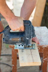 Male carpenter cuts a wooden plank with a jigsaw