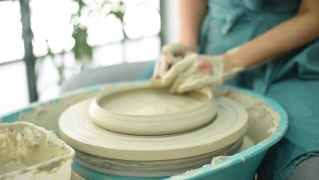 Hands of potter sculpt blank from white clay. Master works on potter's wheel, doing plate.  Workshop for manufacturing potter's products. Concept of creative, skill and handmade.