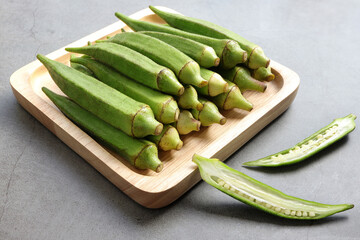 Close up of Fresh okra fruits or abelmoschus esculentus in wooden plate on the table.