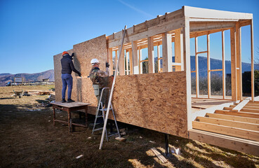 Carpenters mounting wooden OSB panel on the wall of future cottage. Men workers building wooden...