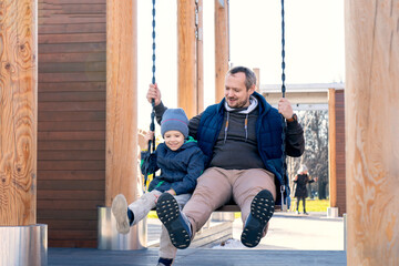 Dad and son ride on a swing together. Laughter and joy, family