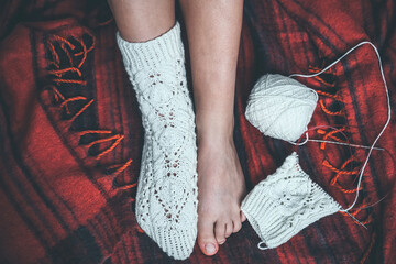 Knitted golf socks on the girl's legs and knitting with knitting needles and a ball on a red plaid.