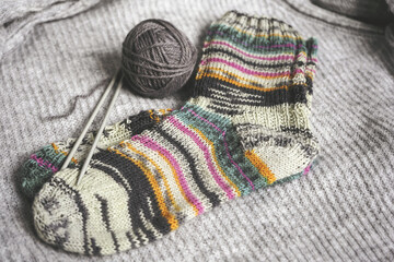 Knitted striped socks and knitting needles with a ball on a red plaid.