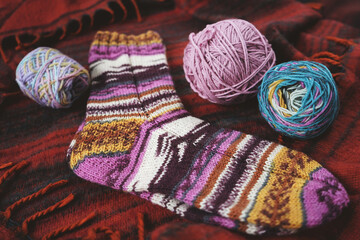 Knitted striped socks and knitting needles with a ball on a red plaid.