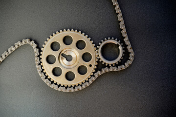 Gears from a car engine and a chain on a dark background.