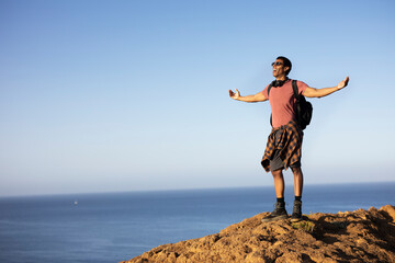 Young man standing on the stone with raised up arms. Tourist man on the top of the mountain