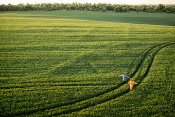 Aerial view on green wheat field with couple walking on pathway on sunset. People enjoy nature on farmland. Wide landscape with copy space © rh2010