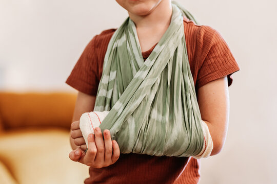 Crop child putting broken arm in sling