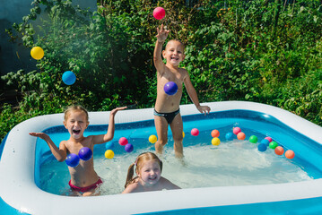 Three happy friends are splashing in an inflatable pool in the garden. Concept of summer season and...