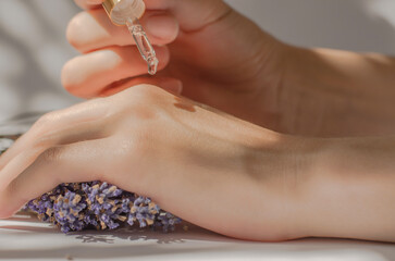 Female hands hold a pipette with lavender oil. Lavender oil dripping from a pipette on hands,...