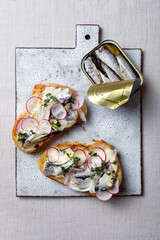 Grilled bread toast with mayonnaise, sardines, radish and marinated fennel. Open tin of sardines, sardine toast on serving board