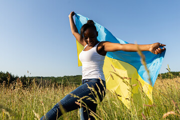 African american woman wrapped in ukrainian yellow blue flag flutters waving in the wind. National...