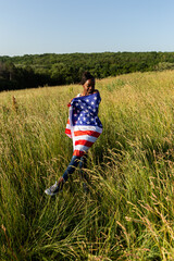 African american woman wrapped in american flag flutters waving in the wind. Happy 4th of July! Independence Day celebrating. Stars and stripes. Freedom concept.
