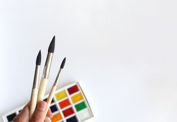 Three art brushes in hand and multicolored watercolors on a white background. Place for text