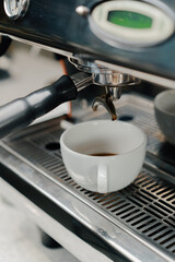 Pouring coffee flow from a professional machine into a cup. The barista makes a double espresso using a filter holder. Flowing fresh ground coffee. Drinking roasted black coffee in the morning