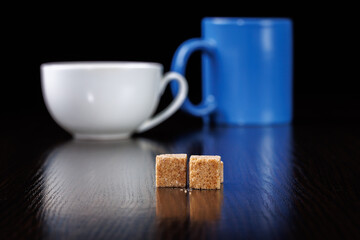 Two cubes of brown sugar on the background of a cup and mug. Selective focus.