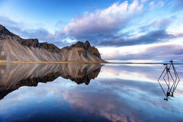 Vestrahorn reflected in shallow waters, Southern Iceland. Two tripods are set to take photographs.