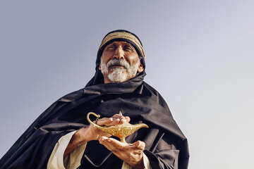 An old Arabic sorcerer holds an Aladdin's lamp and conjures.