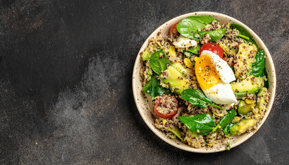 Quinoa buddha bowl with avocado, egg, tomatoes, spinach and sunflower seeds on a dark background....