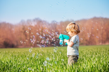 Little blond boy play soap bubbles stand at the spring field