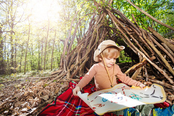 Boy with treasury map playing treasure hunt in hut of branches