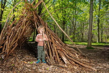 Blond boy with wood pile play in hut of branches
