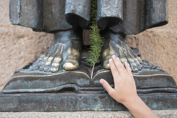 Close up view of hand touching the feet of San Pedro de Alcantara bronze sculpture in Cáceres,...