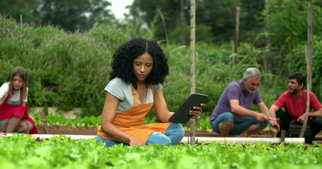 Group of people at urban community farm working at small organic business. One black woman holding tablet
