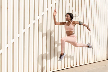 Young African American sporty woman jumping up and running against light background. Female model...