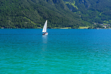 beautiful yacht floats under white sail on picturesque lake Achensee in Austria, green mountains rises above calm expanse of water, concept of vacation by reservoir, water sports, resort place tyrol