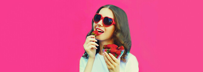 Portrait close up of happy smiling woman with handful of fresh strawberries wearing red heart...
