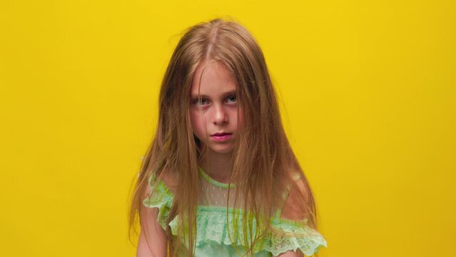 unhappy kid girl disheveled tousled and dirty hair and looking at camera on the yellow background, studio shot. children scalp problems, scratch hair
