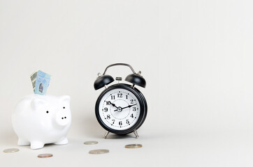 Piggy bank, coins and an alarm clock on a light gray background